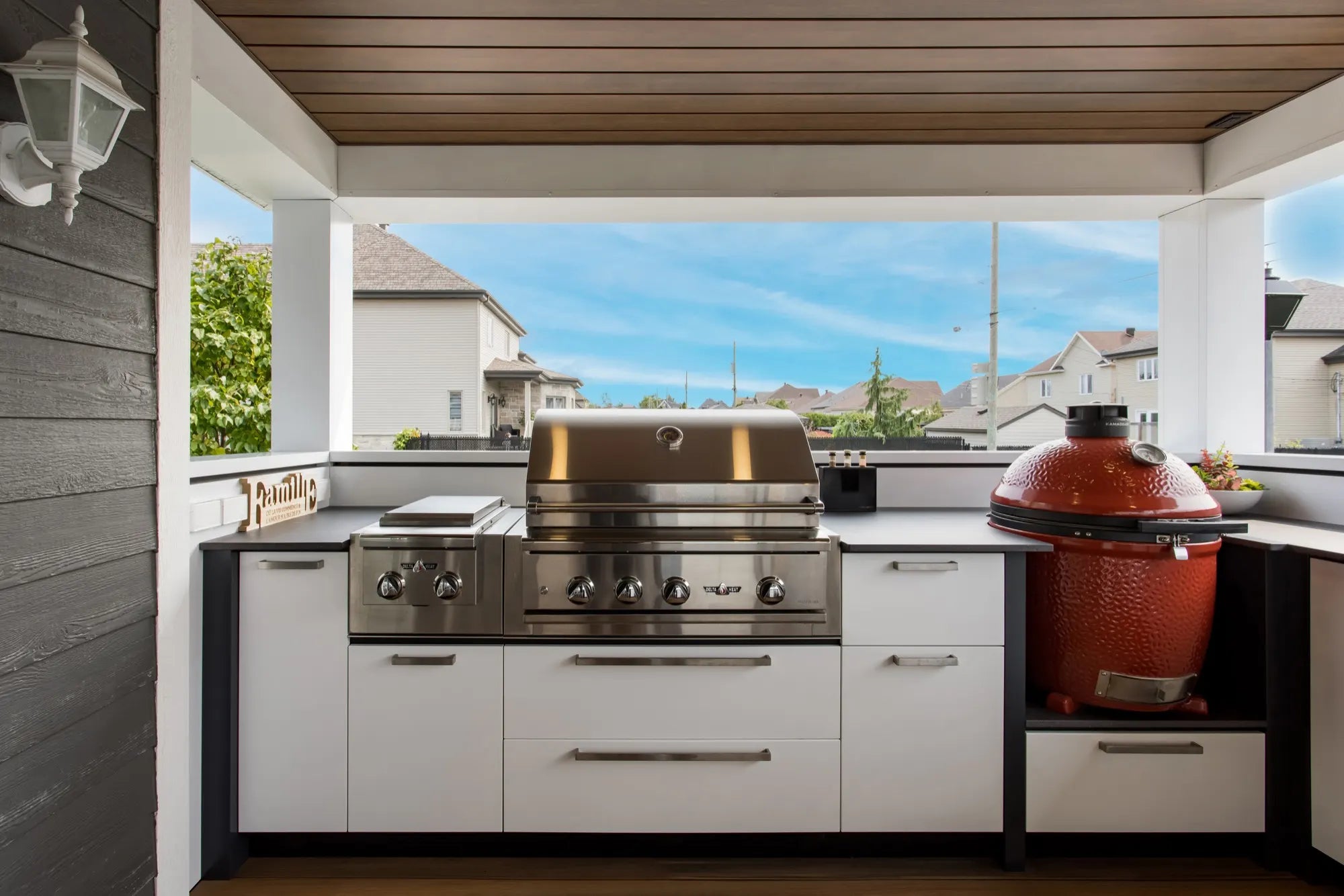 Cuisine extérieure Station Grill blanche avec barbecue encastré et kamado rouge, sous un plafond de bois